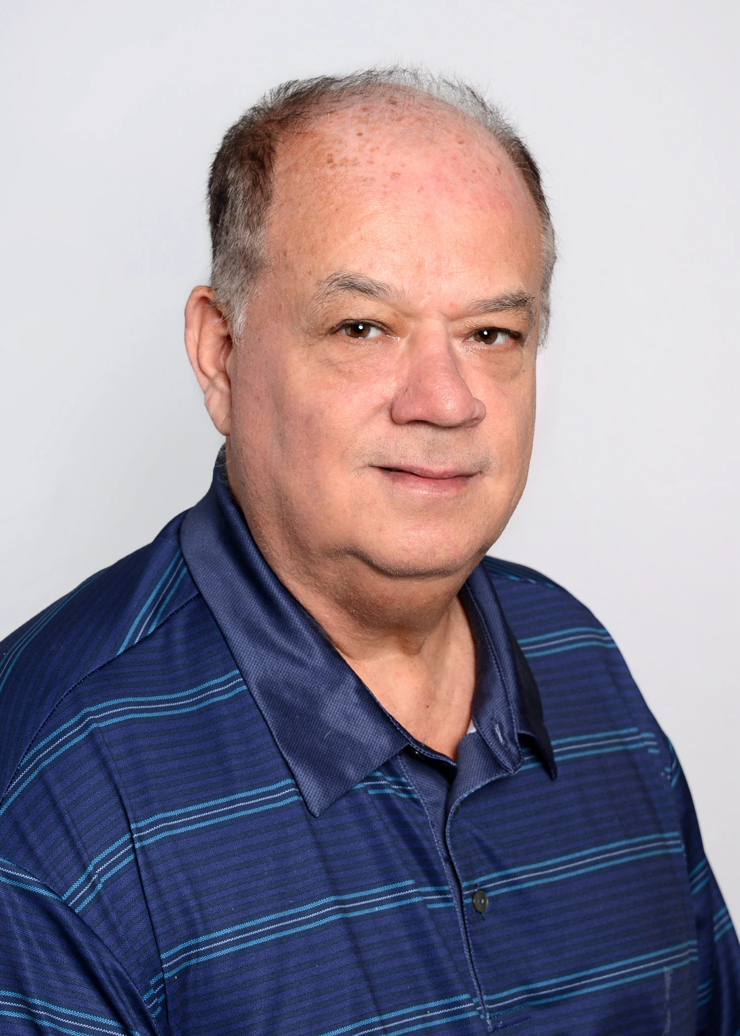 Portrait of a man wearing a blue striped polo shirt against a white background.
