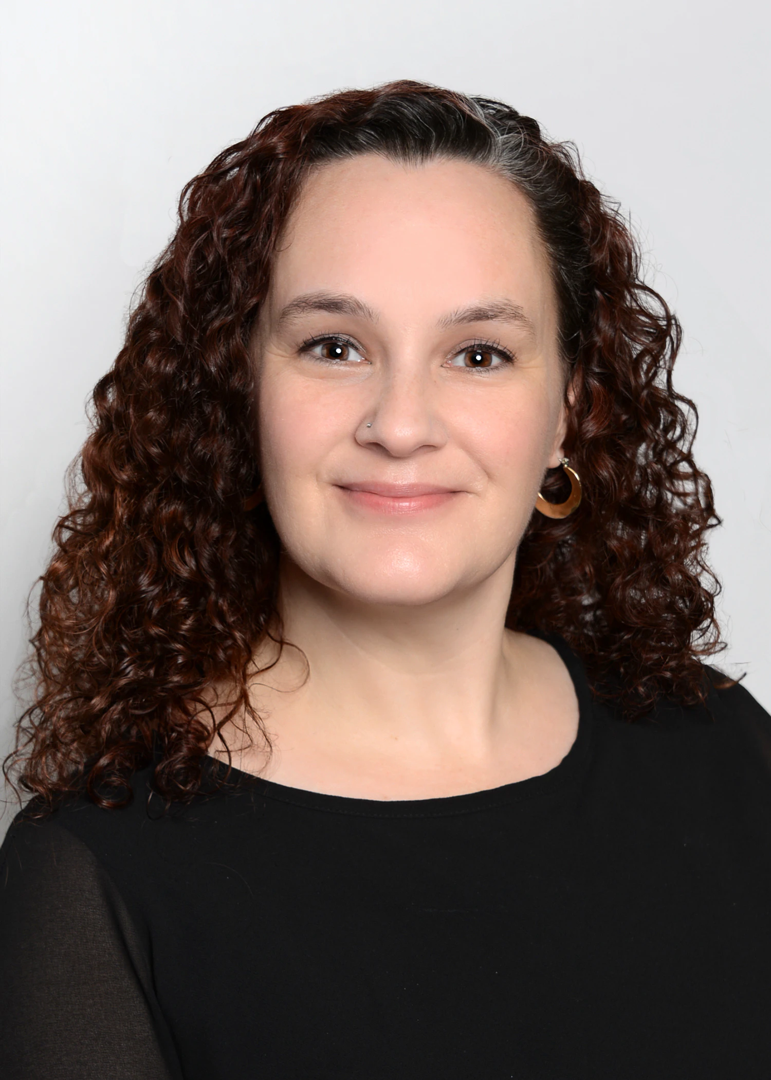 Professional portrait of a person with curly hair wearing a black top against a white background.