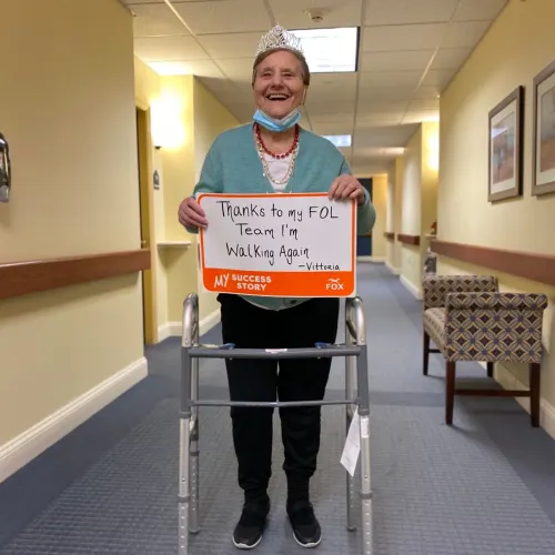 Person with walker holding thank-you sign indoors